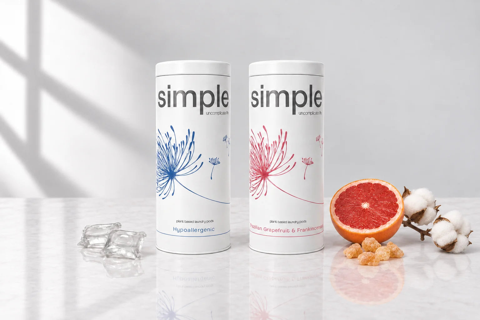 The Hypoallergenic tin and the Brazilian Grapefruit & Frankincense tin standing together, with cotton bolls, a grapefruit half, frankincense resin and two clear pods